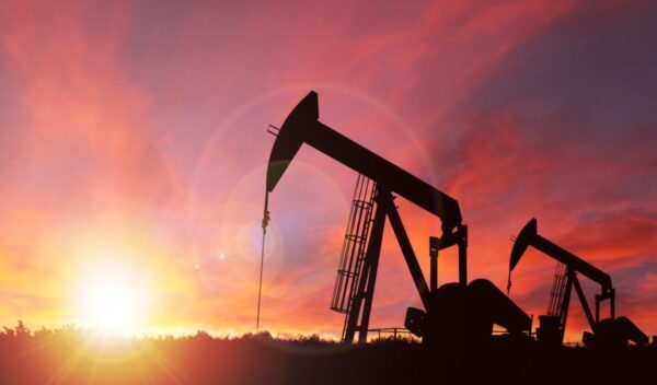 Pumpjack silhouette against a sunset sky with deliberate lens flare and copy space. These jacks can extract between 5 to 40 litres of crude oil and water emulsioin at each stroke. (Pumpjack silhouette against a sunset sky with deliberate lens flare an